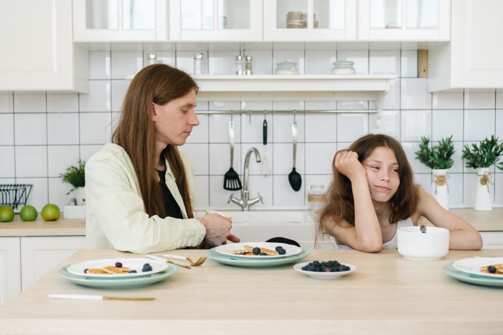 Young girl frowning beside her father at the breakfast table, showing the quiet family distance bad breath can create