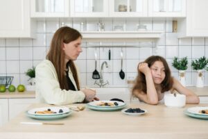 Young girl frowning beside her father at the breakfast table, showing the quiet family distance bad breath can create