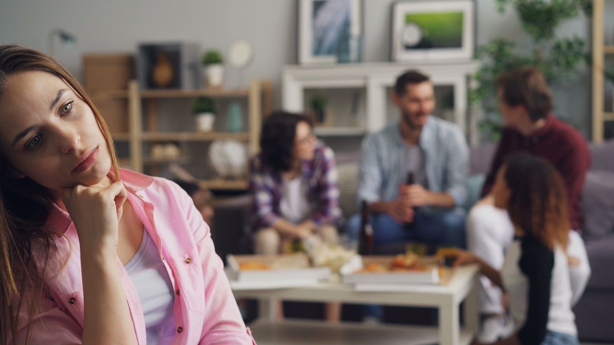 Woman sitting alone while family gathers in background, feeling isolated and left out within family unit