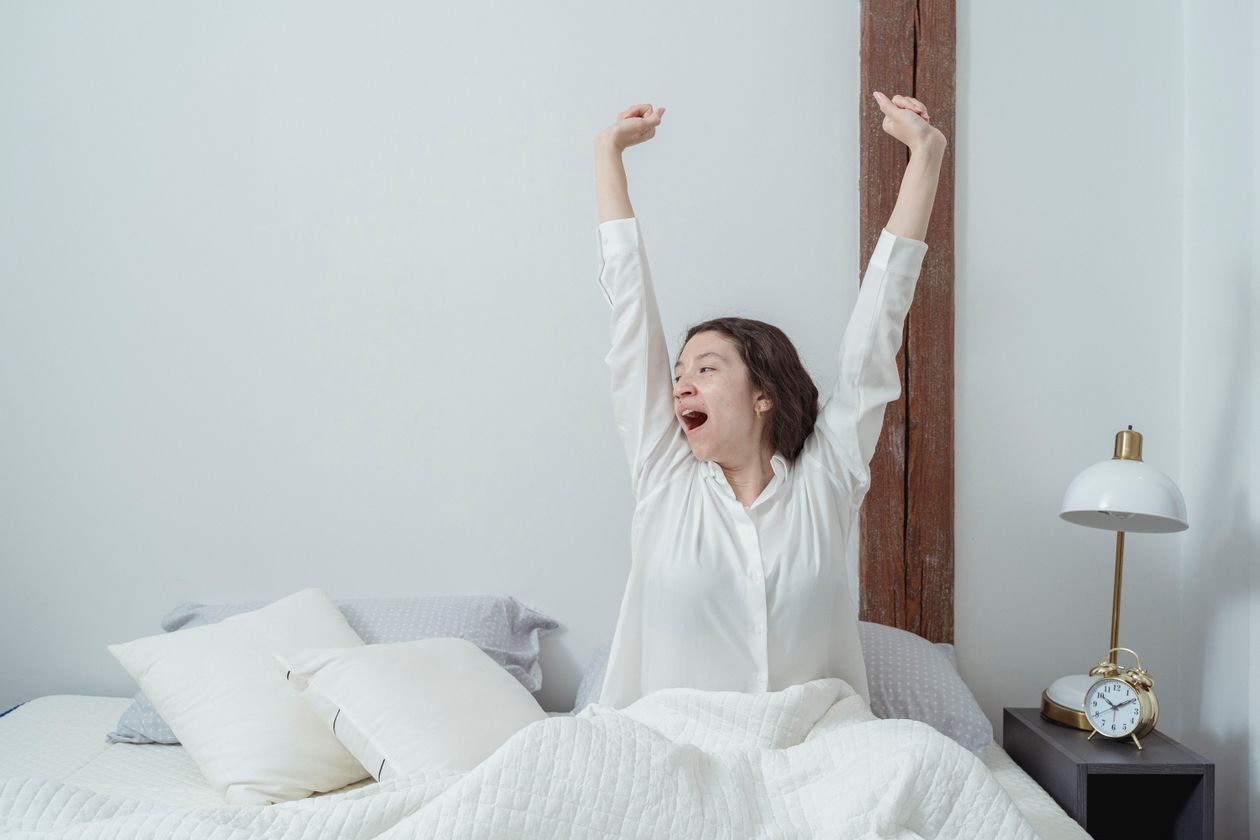 Why Is My Morning Breath So Bad? 1 Young woman awakening in bed in the morning, stretching as she wakes up