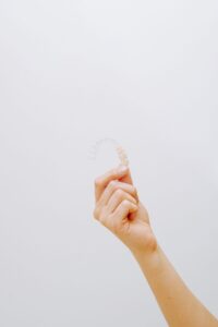 Person holding a clear aligner, which traps bacteria against the teeth and can cause bad breath
