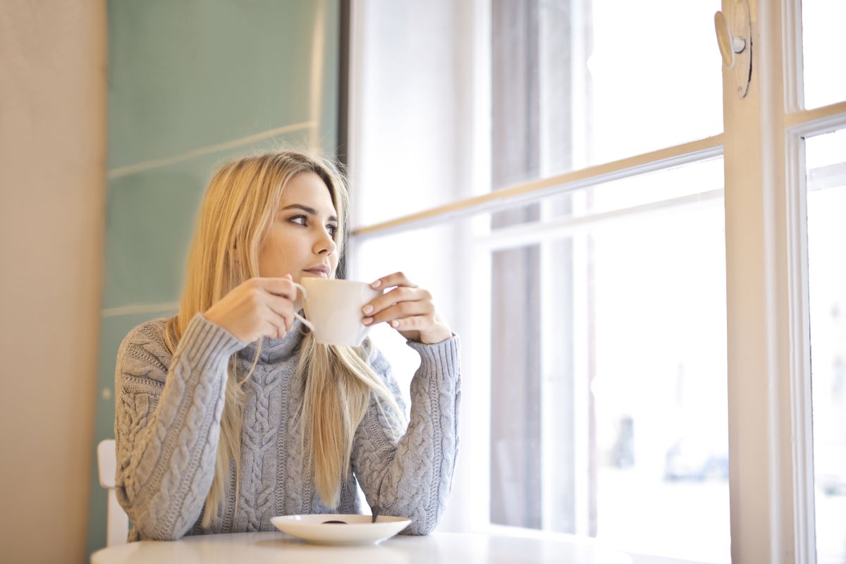 Woman in a knit sweater holding a mug, calm and steady after the embarrassment of bad breath has passed