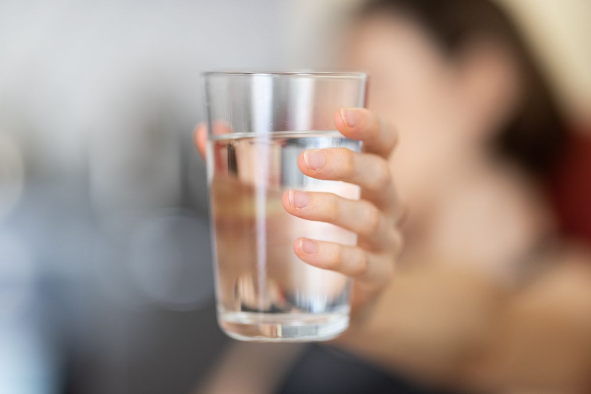 Hand holding a clear glass of water, the simplest remedy for dry mouth and bad breath from medication
