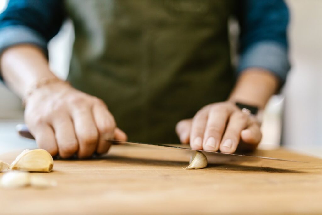 Hands slicing fresh garlic on a wooden cutting board