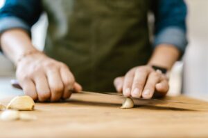 Hands slicing fresh garlic on a wooden cutting board