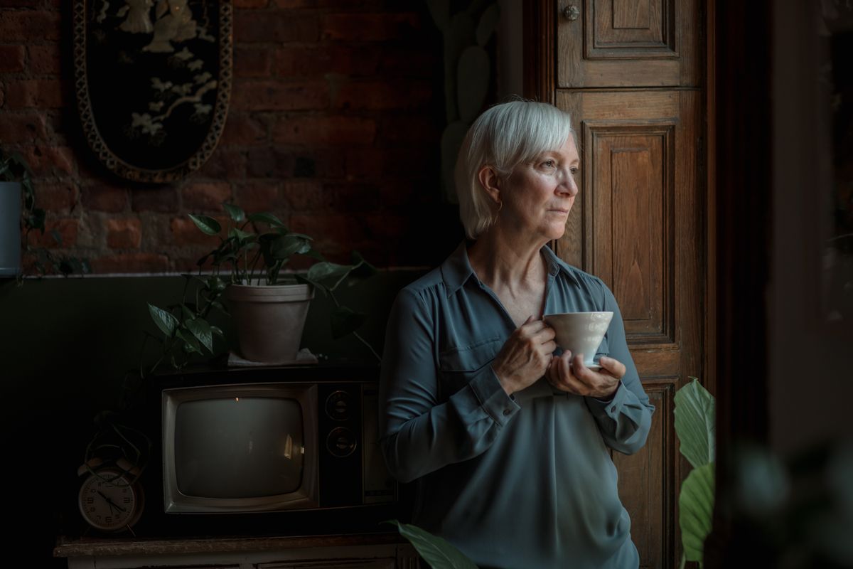 Grey-haired woman holding a warm cup by a window, living with hormonal dry mouth and bad breath after menopause