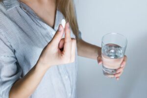 Woman holding a pill and a glass of water, taking daily medication that can cause dry mouth and bad breath