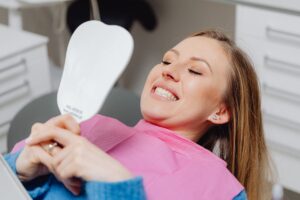 Woman in a dental chair checking her gums in a mirror after an early gum disease diagnosis