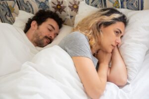 Woman lying awake beside her sleeping partner, dealing with mouth breathing at night bad breath