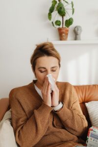 Woman blowing her nose on a sofa, illustrating postnasal drip and bad breath