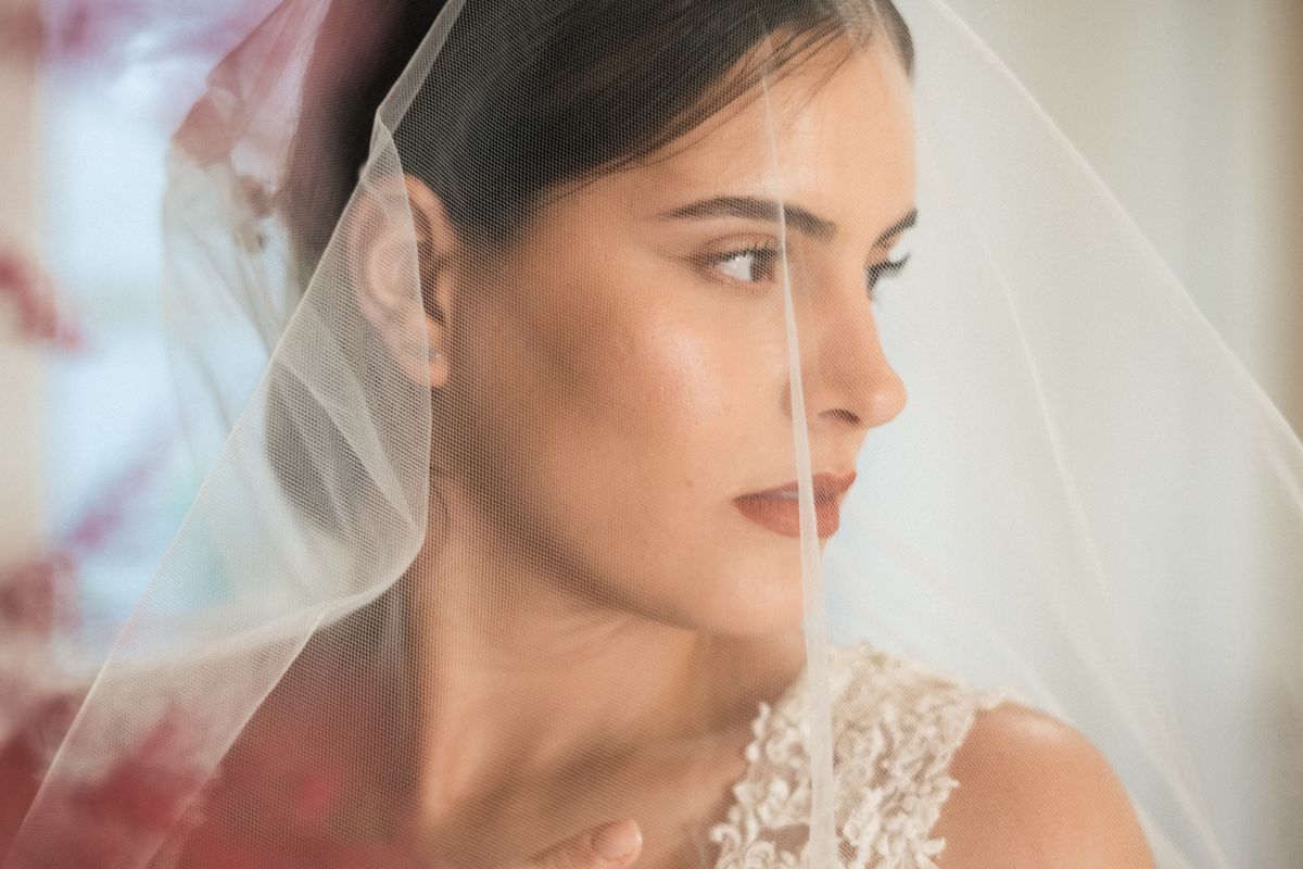 Bride alone behind her veil in soft light, carrying a private worry about bad breath before her wedding day