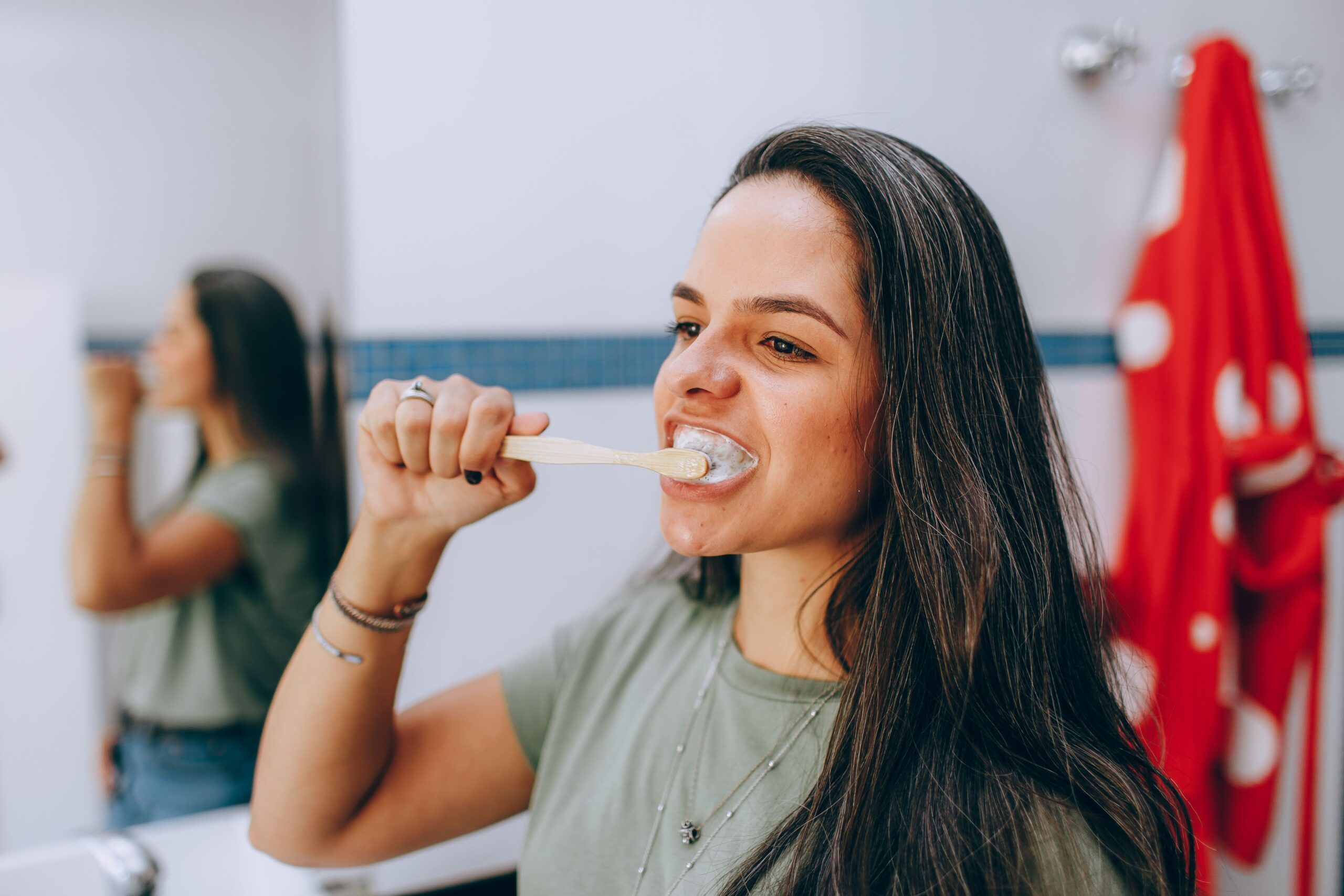 Woman brushing her teeth in a bright bathroom as part of her daily routine after a dental cleaning