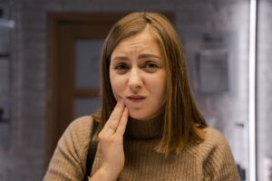 Woman holding her cheek indoors with mouth ulcers that keep coming back
